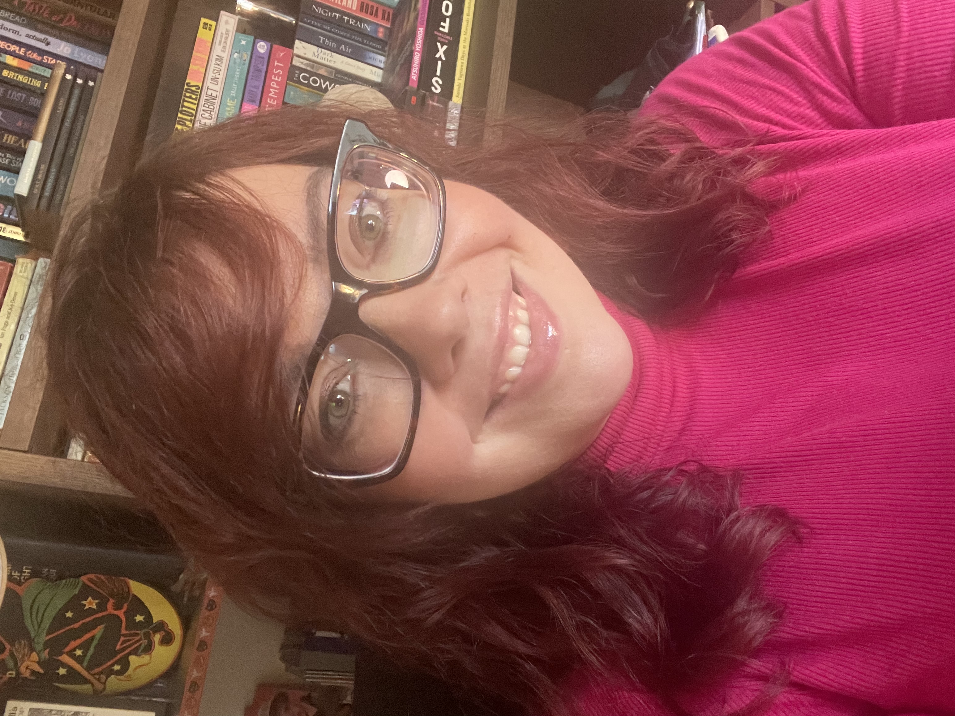 a white woman with red hair, big glasses and a pink top. Alix Armitage, author.