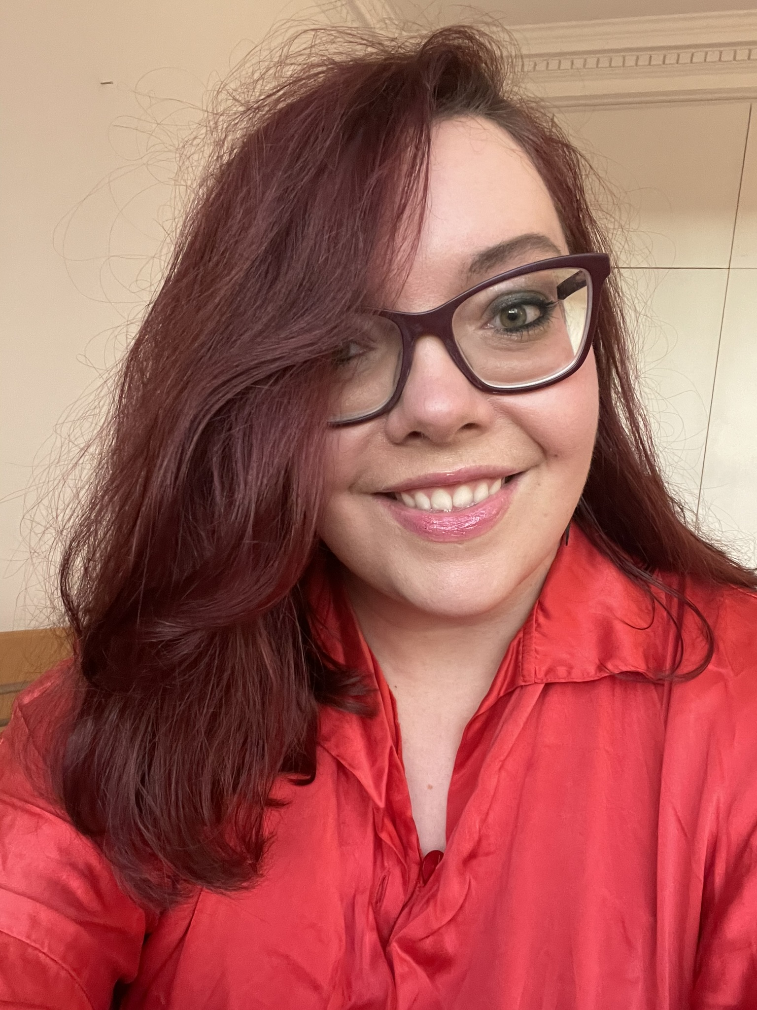 a white woman with red hair, big glasses and a red shirt. Jess Popplewell, author.